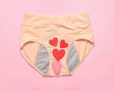 Dönem külotlu kompozisyon, regl kupası ve renkli arka planda kağıt kesiği olan kalpler.