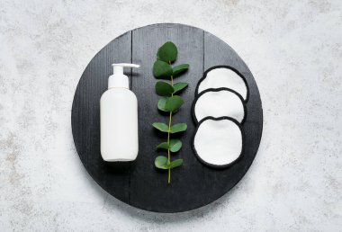 Wooden board with reusable cotton pads, bottle of cosmetic product and eucalyptus branch on light background clipart