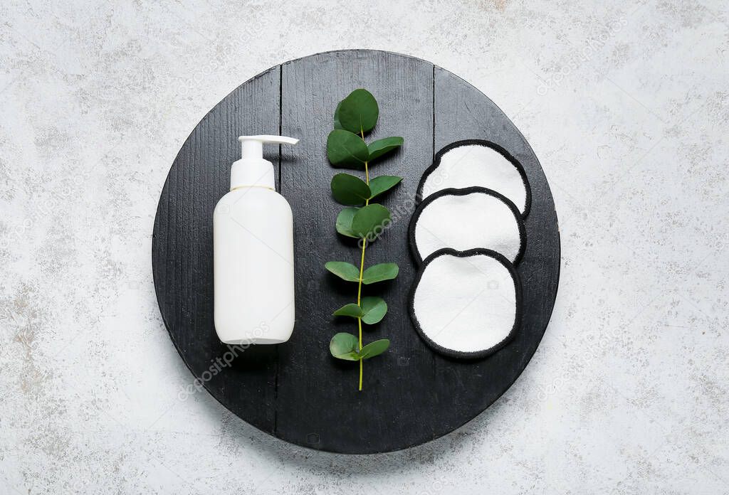 Wooden board with reusable cotton pads, bottle of cosmetic product and eucalyptus branch on light background