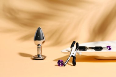 Butt plug and nipple clamps from sex shop on color background