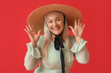 Kırmızı arka planda saman şapkalı mutlu kadın.