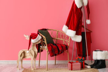 Ekose ve yastıklı sandalye, Noel Baba kostümlü askı ve renkli duvara yakın botlar.