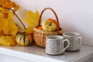 Kabaklı sepet, sarı yapraklar ve şömine rafında ışık duvarının yanında fincanlar.