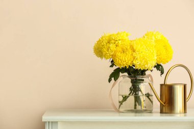 Sarı kasımpatı çiçekli vazo masada, ışık duvarına karşı.