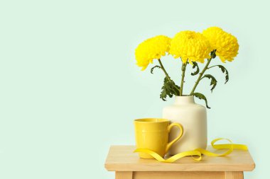 Sarı kasımpatı çiçekli vazo ve mavi duvara karşı duran bardak.