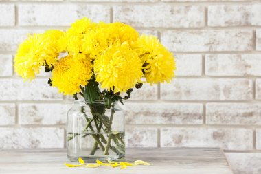 Sarı kasımpatı çiçekli vazo tuğla duvara karşı.