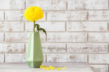 Sarı kasımpatı çiçekli vazo tuğla duvara karşı.