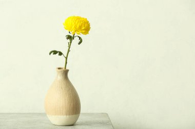 Sarı kasımpatı çiçekli vazo masanın üzerinde, ışık duvarının karşısında.