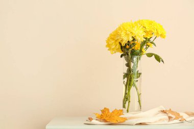 Sarı kasımpatı çiçekli vazo masada, ışık duvarına karşı.