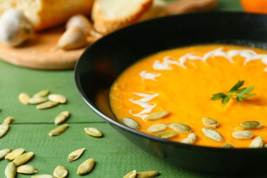 Lezzetli balkabağı kremalı çorba ve renkli ahşap arka planda tohumlar, yakın plan.