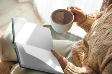 Elinde bir fincan lezzetli çay ve boş sayfalarla kitap okuyan genç bir kadın.