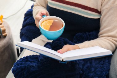 Oturma odasında çay içip kitap okuyan bir kadın.