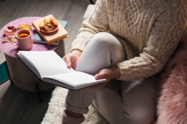 Oturma odasında açık bir kitapla kanepede oturan kadın.