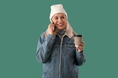 Kahveli olgun bir kadın, arka planda cep telefonuyla konuşuyor.