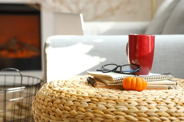 Bir fincan çay, gözlük, defterler ve sonbahar balkabağıyla hasır bir kanepe.