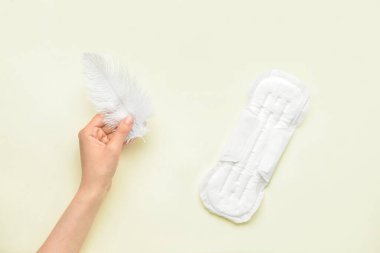 Sarı arka planda tüy ve regl pedi olan bir kadın eli.