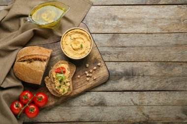 Tahta arka planda lezzetli humus, ekmek ve domateslerle dolu bir kase.