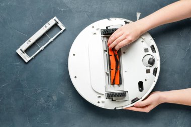 Koyu arkaplanda modern robot süpürgesi olan kadın eller.