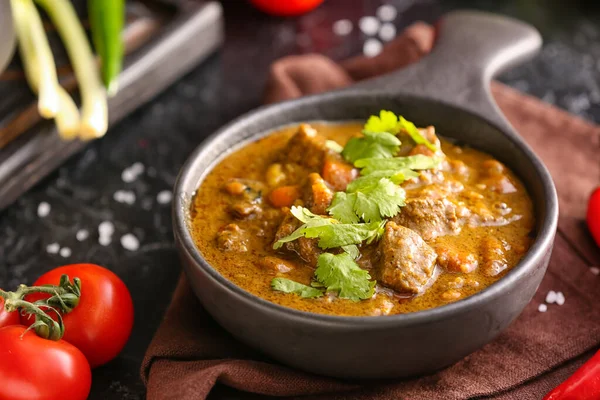 Frying pan with tasty beef curry on dark background