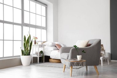 Koltuğu ve pencere kenarındaki ahşap komodinli şık bir yatak odası.