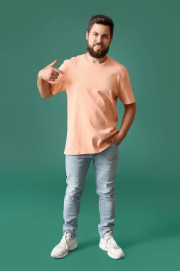 Yeşil arkaplanda bej tişörtü gösteren yakışıklı bir adam.