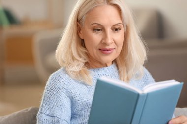 Evde kitap okuyan güzel olgun bir kadın.