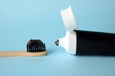 Siyah diş macunlu bambu fırçası ve mavi arka planda tüp.