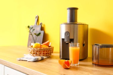 Mutfaktaki masada taze narenciye ve bir bardak meyve suyu ile modern meyve sıkacağı.