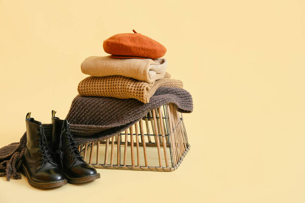 Basket with stylish winter clothes on light background