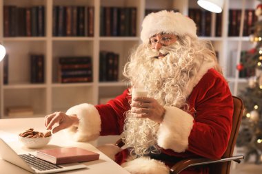 Noel Baba akşam evde lezzetli kurabiyeler ve süt yiyor.