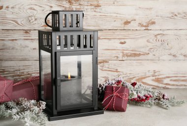 Yanan mumlu siyah Noel feneri, hediye kutuları ve hafif ahşap arka planda köknar dalları.