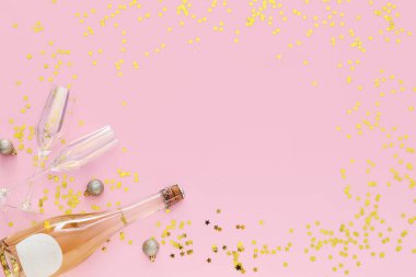 Altın konfetiden yapılmış çerçeve. Noel topları, şampanya şişesi ve pembe arka planda gözlük.