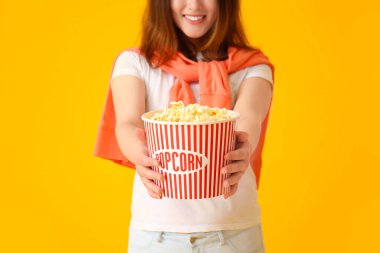 Sarı arka planda bir kova lezzetli patlamış mısırlı genç Asyalı kadın.