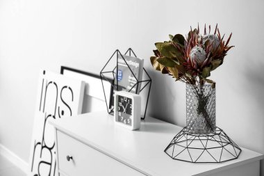 Çiçekli vazo, şarjör ve saat ışıklı duvarın yanında.