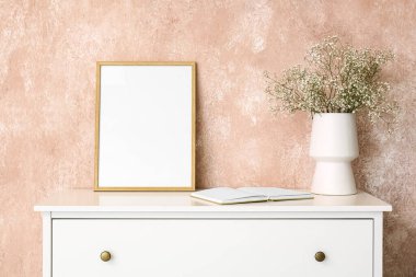 İçinde çingene çiçekleri olan vazo, pembe duvarın yanındaki rafta kitap ve çerçeve.