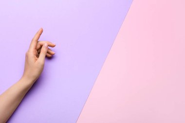 Manikürlü bir kadın eli. Renkli arka plandaki bir şeyi işaret ediyor.
