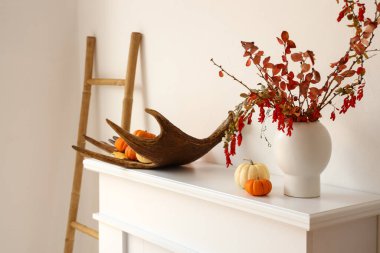 Ağaç dalları, geyik boynuzu ve şömine rafında ışık duvarı yakınında balkabakları olan vazolar.