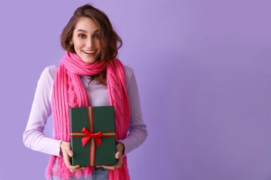 Kış kıyafetleri içinde şık genç bir kadın ve renkli arka planda bir Noel hediyesi.