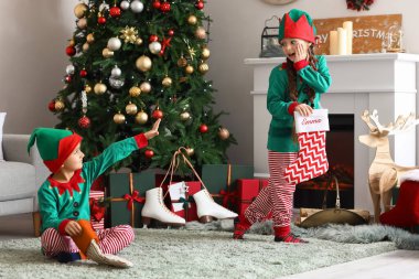 Elf kostümlü şirin çocuklar ve oturma odasında Noel çorapları.