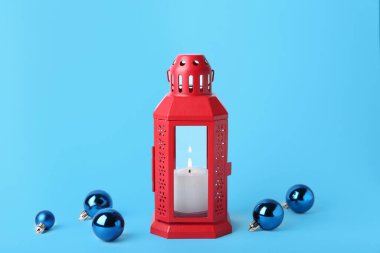 Yanan mum ve mavi arka planda topları olan Noel feneri.