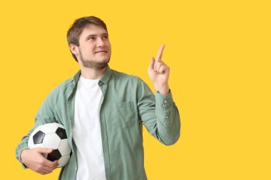 Futbol topuyla yakışıklı bir adam arka plandaki bir şeyi işaret ediyor.