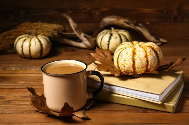 Bir fincan lezzetli kahve, ahşap arka planda kitaplar ve balkabakları.