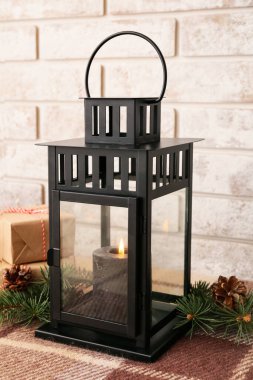 Yanan mumlu siyah Noel feneri, tuğla duvarın yanındaki masada köknar dalları ve koniler