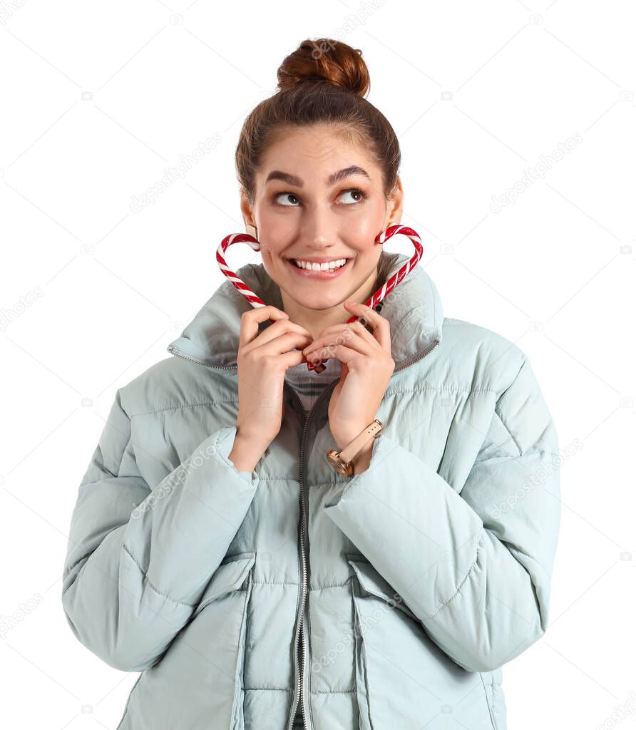 Happy young woman in winter clothes and with candy canes on white background