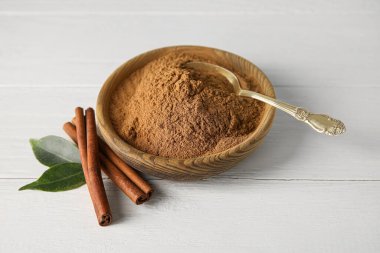 Tarçın tozlu kase ve beyaz ahşap arka planda çubuklar