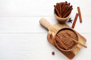 Tarçın tozlu kase ve beyaz ahşap arka planda çubuklar