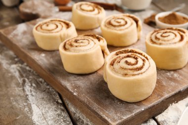 Ahşap arka planda pişmemiş tarçın ruloları olan tahta, yakın plan.