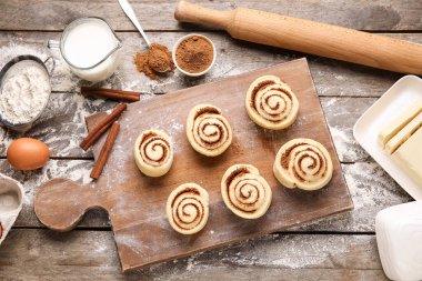 Pişmemiş tarçınlı rulo ve ahşap arka planda malzemeler.