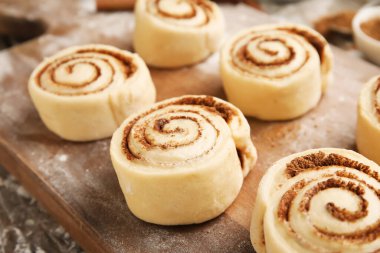 Ahşap arka planda pişmemiş tarçın ruloları olan tahta, yakın plan.