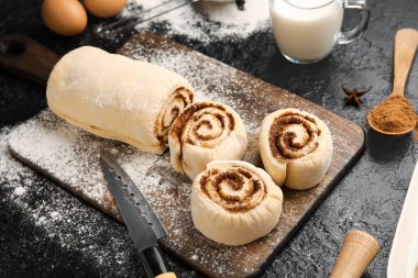 Tahta tahta tahta, siyah arka planda pişmemiş tarçın ruloları.